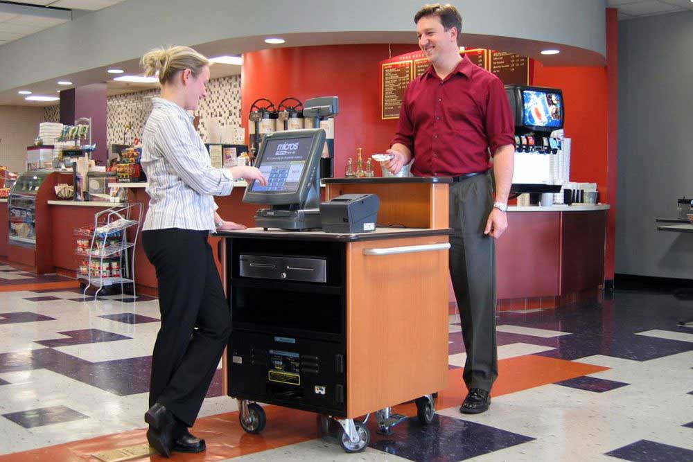 One of our POS powered carts for hotel & Hospitality being used in the middle of a hotel cafeteria, with a person happily paying.