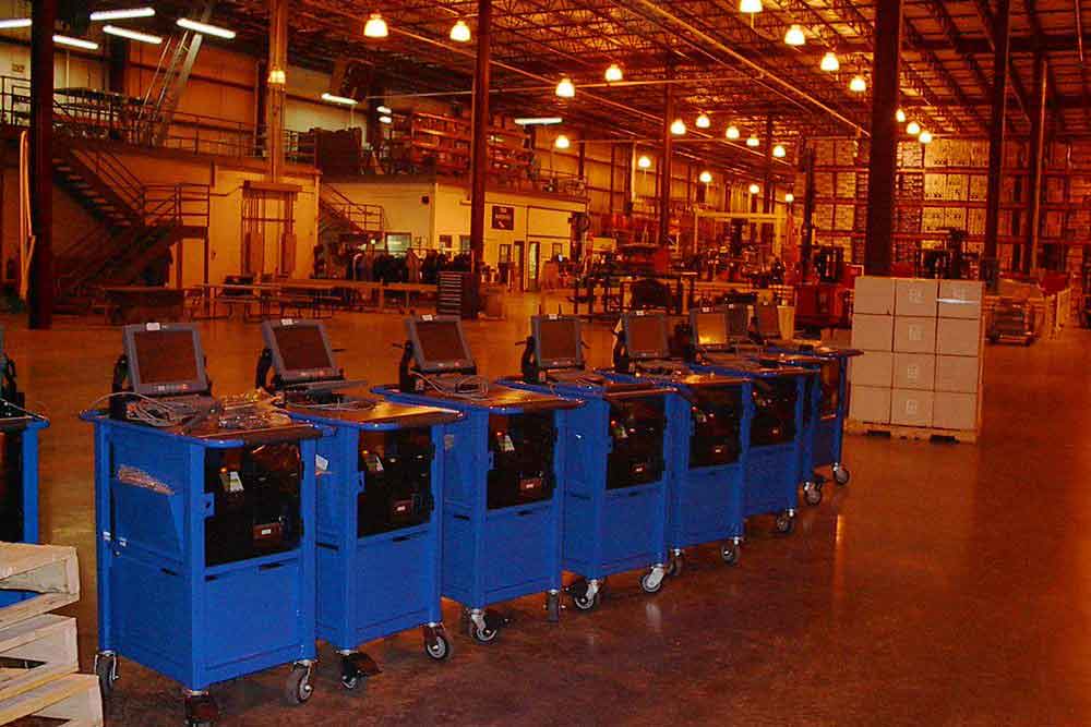 Eight of our powered carts for manufacturing lined up in a factory with a laptop on top.